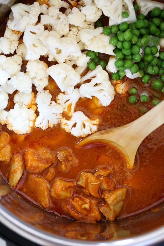 This Instant Pot Chicken Tikka Masala with cauliflower and peas is a lightened up, dairy-free version of the classic Indian curry. A wooden spoon stirring cauliflower and peas into tikka masala