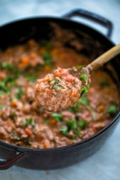 Close up of a spoonful of bolognese sauce held over a pot of sauce.