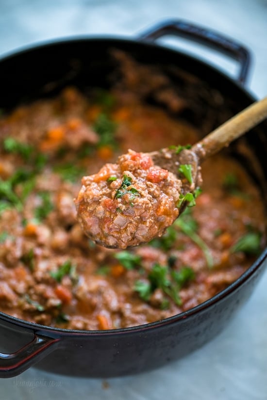 Close up of a spoonful of bolognese sauce held over a pot of sauce.