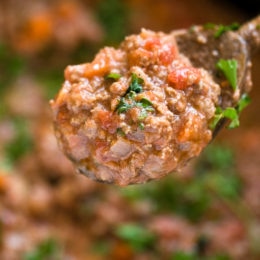 Close up of a spoonful of bolognese sauce held over a pot of sauce.