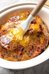 Brushing glaze onto ham in slow cooker.