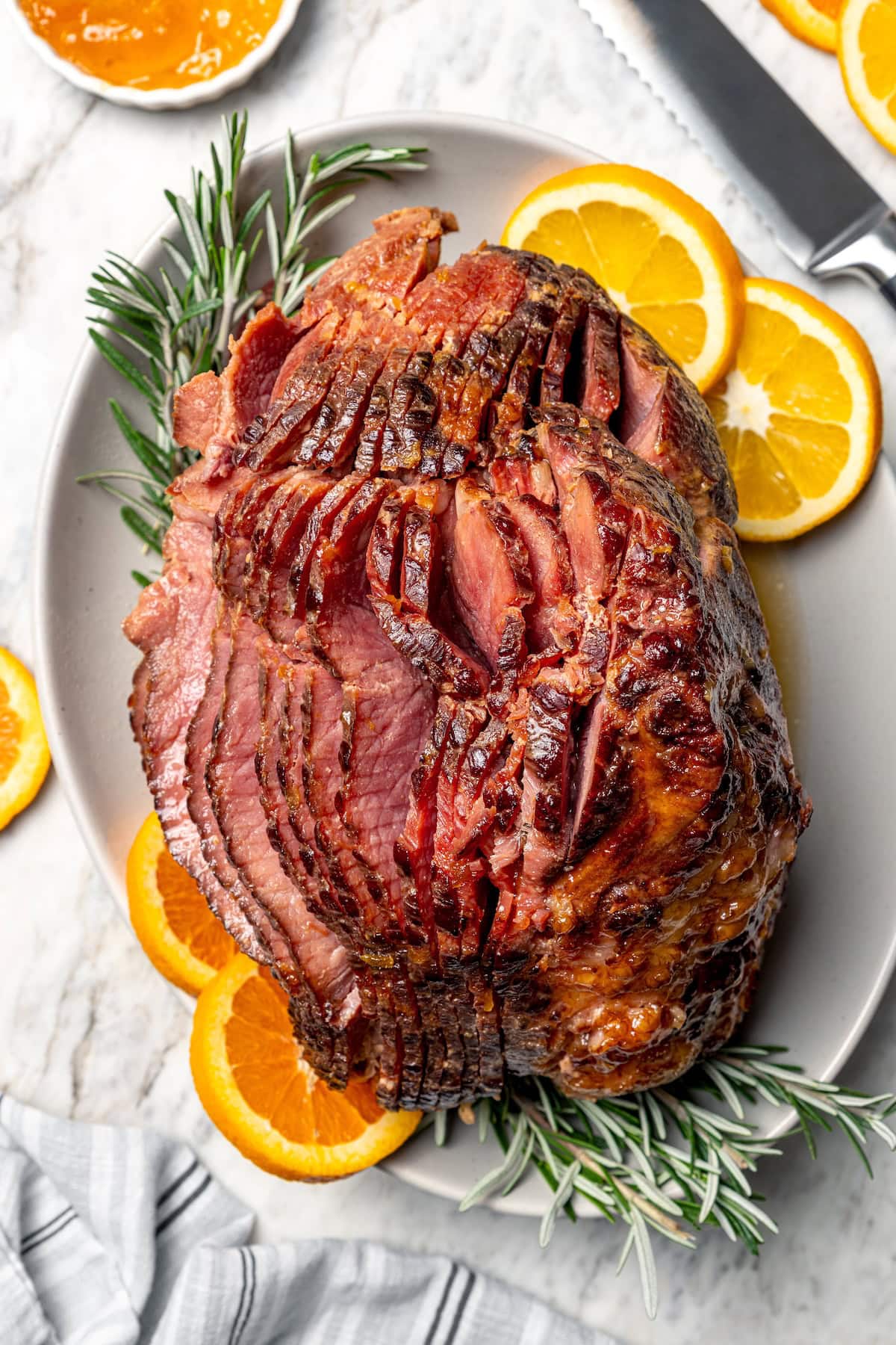 Slow Cooker Ham is the easiest main dish for the holidays! A two-ingredient glaze and a crockpot are all you need for moist, flavorful ham. Glazed spiral slow cooker ham on platter with rosemary and orange slices.