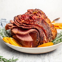 Slow cooker spiral ham on platter with sprigs of rosemary and orange slices.