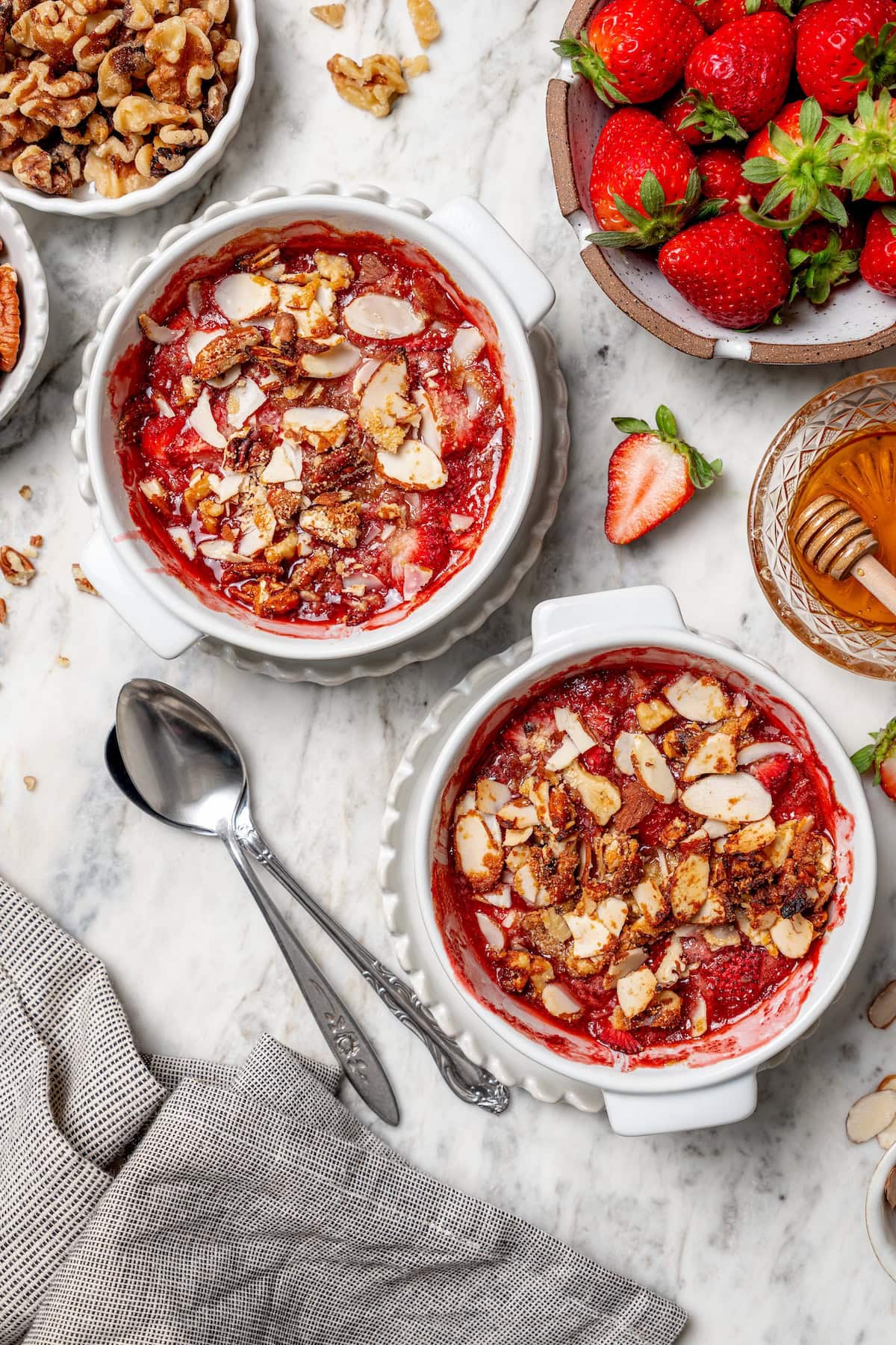 This healthy strawberry crisp recipe is perfectly portioned into individual servings, with a delicious nutty topping. So easy to make too! Overhead view of two strawberry crisps in ramekins
