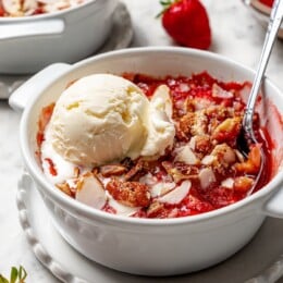 Scoop of vanilla ice cream on top of strawberry crisp in bowl