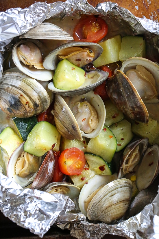 Grilled little neck clams cooked in foil packets with zucchini and tomatoes in a garlic white wine sauce, so fast and easy, perfect to make all summer long!