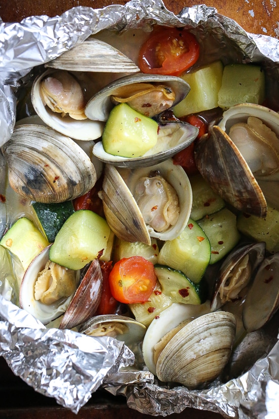 Grilled little neck clams cooked in foil packets with zucchini and tomatoes in a garlic white wine sauce, so fast and easy, perfect to make all summer long!