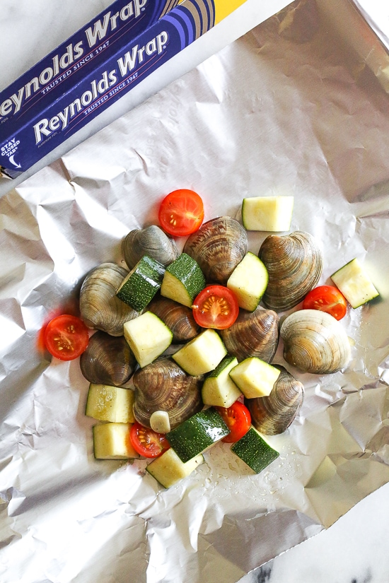 Grilled little neck clams cooked in foil packets with zucchini and tomatoes in a garlic white wine sauce, so fast and easy, perfect to make all summer long!