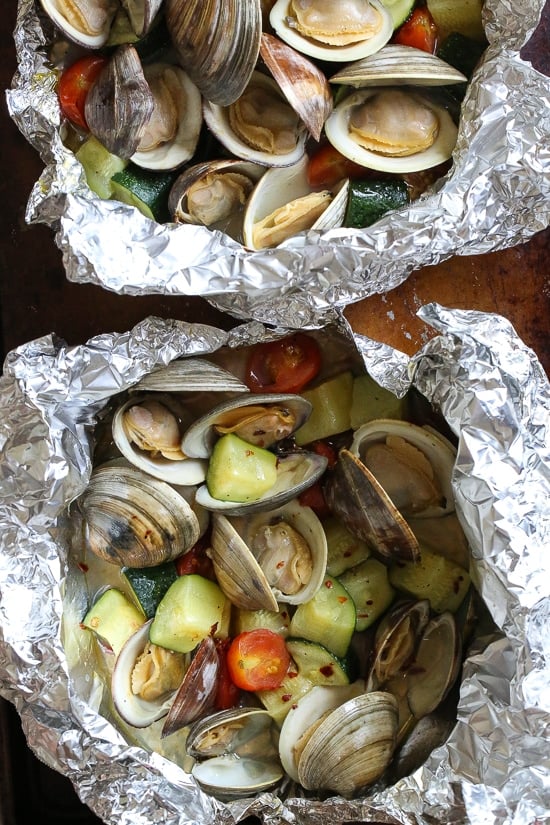 Grilled little neck clams cooked in foil packets with zucchini and tomatoes in a garlic white wine sauce, so fast and easy, perfect to make all summer long!