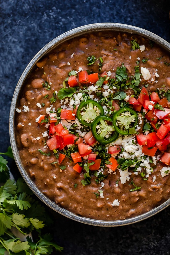 These Instant Pot Refried Beans are a simple, healthy, and fat-free version of the classic Mexican side dish. No oil or lard required! Overhead view of a bowl of Instant pot refried beans with jalapeno and diced tomato