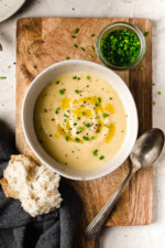 Overhead view of bowl of potato leek soup with small bowl of chives and piece of bread