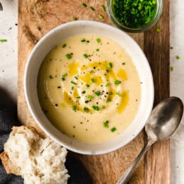 Overhead view of bowl of potato leek soup with small bowl of chives and piece of bread