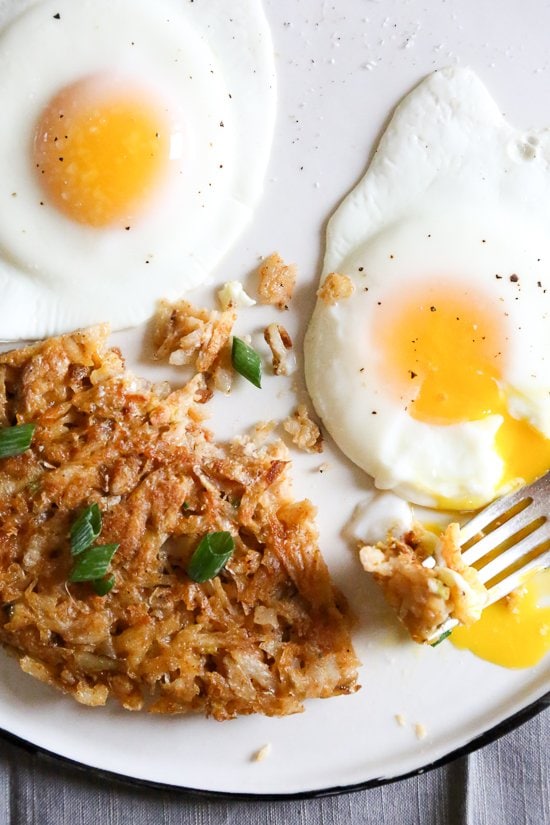 Here's how to make hash browns that are beautifully browned, always crispy, and perfectly seasoned. This recipe won't let you down! Overhead view of hash browns on plate with fried eggs