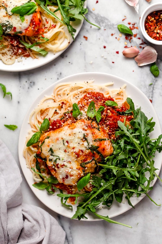 This quick and easy Instant Pot Chicken Parmesan is ready in minutes, with no breading or frying. Perfect for busy weeknights! Overhead view of two plates of Instant Pot chicken parm with spaghetti noodles and greens