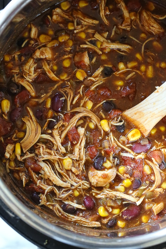 This easy and healthy Instant Pot Chicken Taco Chili is made with chicken, beans, corn and tomatoes and taco seasoning. Chicken taco chili in the Instant Pot being stirred by a wooden spoon