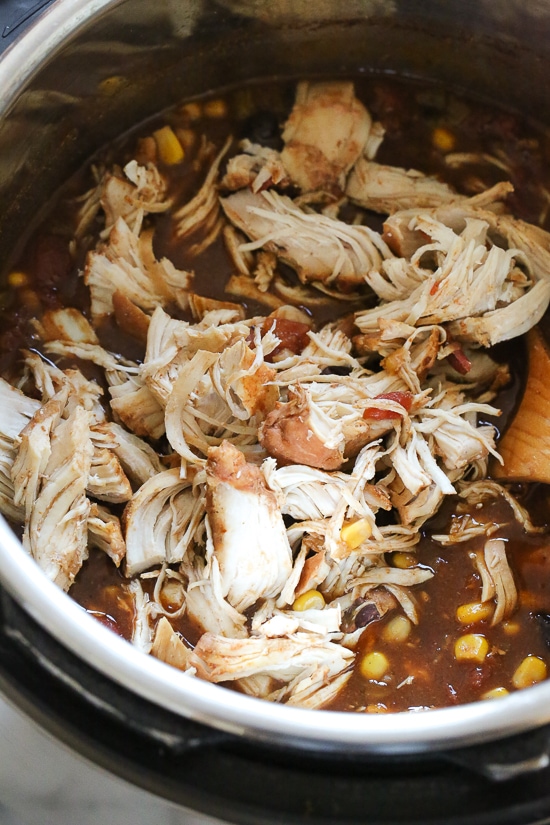 This easy and healthy Instant Pot Chicken Taco Chili is made with chicken, beans, corn and tomatoes and taco seasoning. Shredded chicken being stirred into easy taco chili