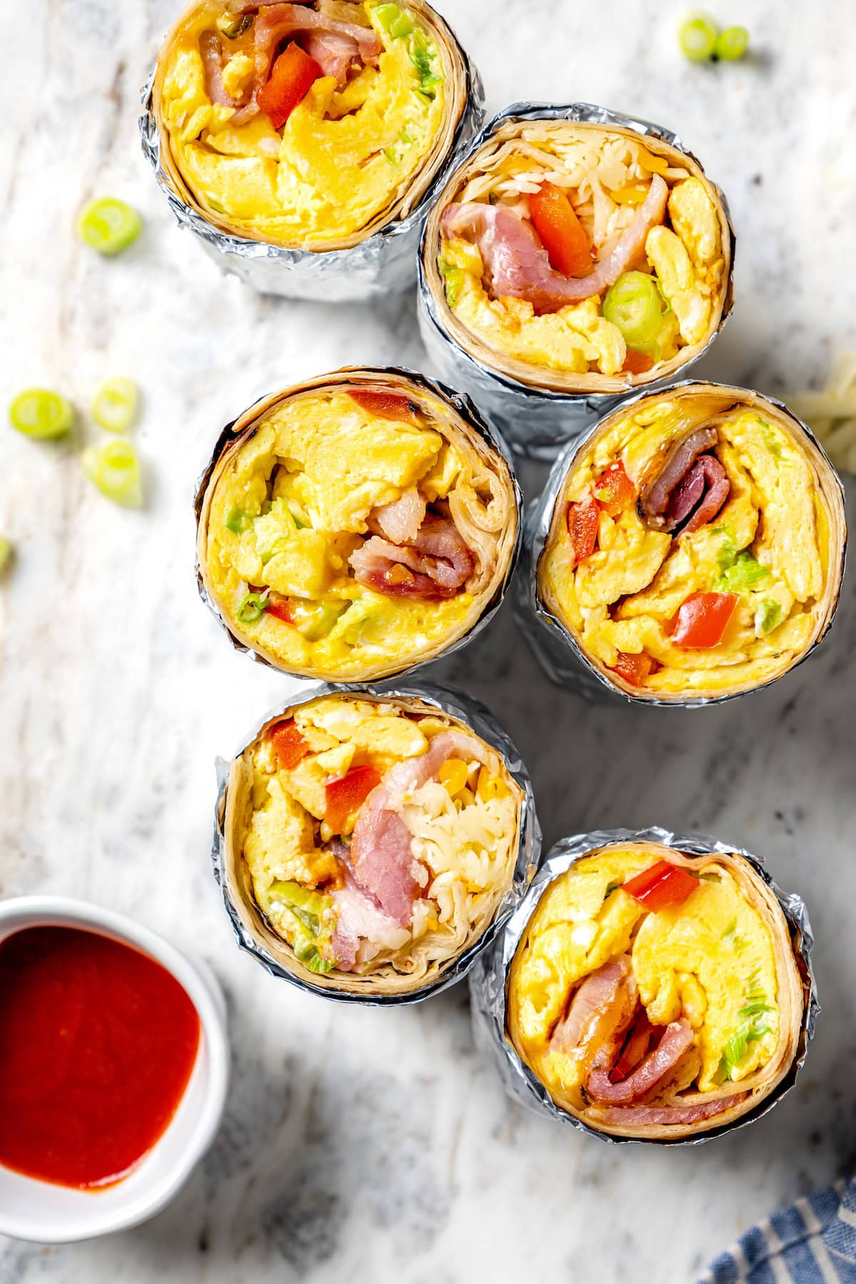 These easy freezer breakfast burritos are a delicious, protein-packed way to start the day with scrambled eggs, veggies, bacon and cheese. Breakfast burritos sliced in half to show fillings