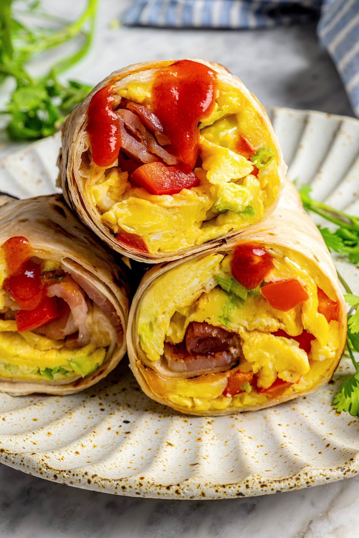 These easy freezer breakfast burritos are a delicious, protein-packed way to start the day with scrambled eggs, veggies, bacon and cheese. Freezer breakfast burritos stacked on plate