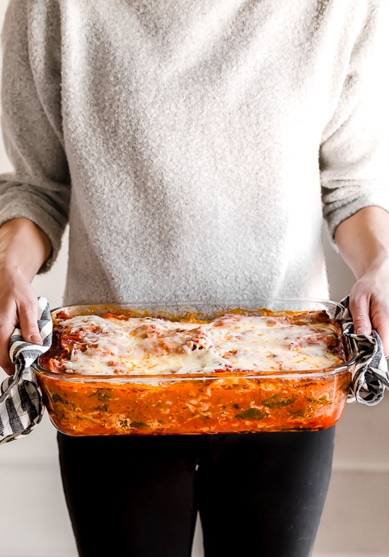 This easy Chicken Parmesan Lasagna is a combination of two classic dishes. It's the perfect family-friendly dish to feed a large crowd! A woman holding a casserole dish of chicken parmesan lasagna
