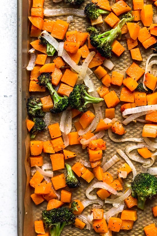 This easy Buddha bowl pairs a brown rice base with roasted broccoli, butternut squash, creamy avocado, fried eggs, and pecans. So delicious! Overhead view of roasted broccoli, butternut squash, and onions on pan