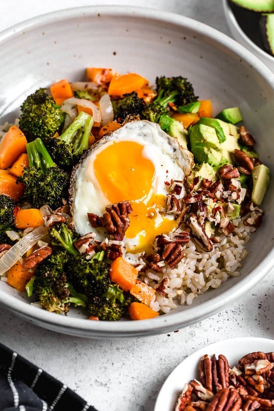 This easy Buddha bowl pairs a brown rice base with roasted broccoli, butternut squash, creamy avocado, fried eggs, and pecans. So delicious! Buddha bowl with brown rice, vegetables and fried egg