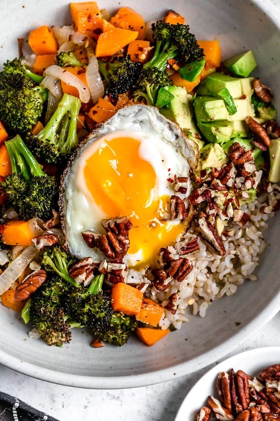 This easy Buddha bowl pairs a brown rice base with roasted broccoli, butternut squash, creamy avocado, fried eggs, and pecans. So delicious! Overhead view of Buddha bowl with fried egg