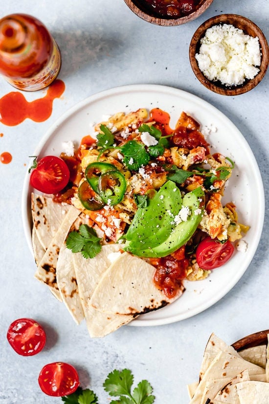 Migas are a classic Tex Mex breakfast recipe, but you can enjoy them anytime of day! Eggs, tortillas, cheese and veggies make them satisfying. Overhead view of migas on plate with tortillas and avocado
