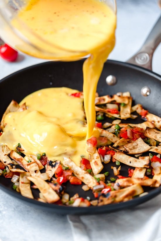 Migas are a classic Tex Mex breakfast recipe, but you can enjoy them anytime of day! Eggs, tortillas, cheese and veggies make them satisfying. Pouring egg into pan for migas