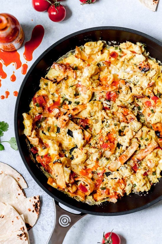 Migas are a classic Tex Mex breakfast recipe, but you can enjoy them anytime of day! Eggs, tortillas, cheese and veggies make them satisfying. Overhead view of migas in skillet before garnishing