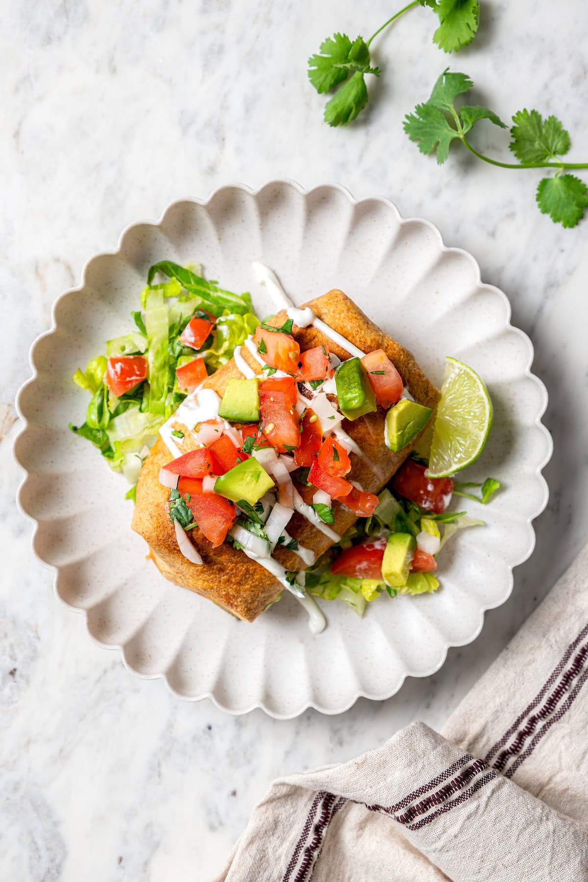 Crispy air fryer chicken chimichangas are an easy and healthier twist on the classic! Filled with cheese, green chiles, and seasoned chicken. Overhead view of chicken chimichanga on plate with lettuce and toppings