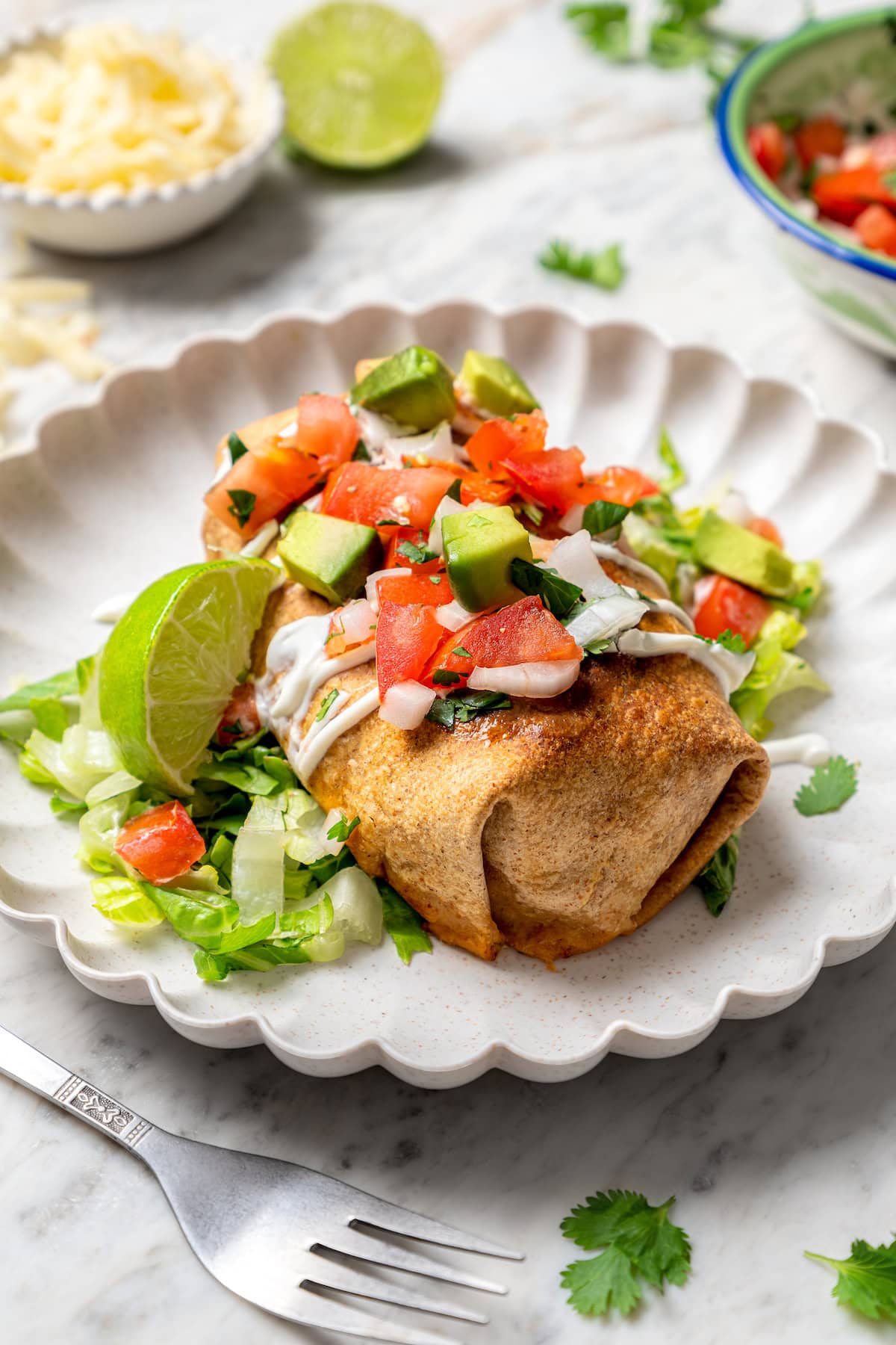 Crispy air fryer chicken chimichangas are an easy and healthier twist on the classic! Filled with cheese, green chiles, and seasoned chicken. Crispy air fryer chicken chimichanga on plate with toppings