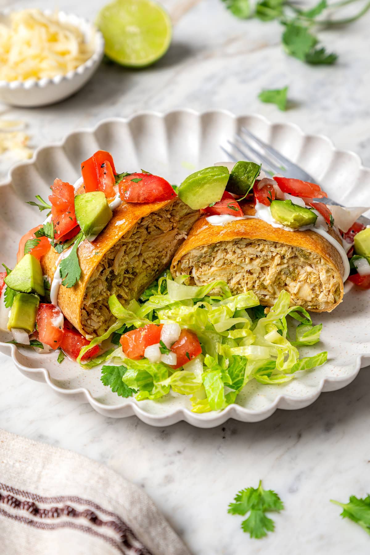 Crispy air fryer chicken chimichangas are an easy and healthier twist on the classic! Filled with cheese, green chiles, and seasoned chicken. Air fryer chicken chimichanga cut in half on plate with lettuce and toppings