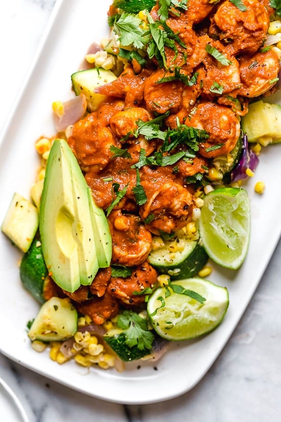This delicious Mexican Shrimp dish is made with saucy Chipotle shrimp served over a bed of corn, zucchini, and red onions, and served with a side of avocado.