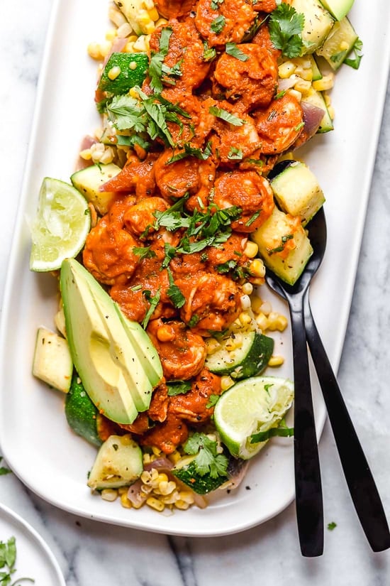 This delicious Mexican Shrimp dish is made with saucy Chipotle shrimp served over a bed of corn, zucchini, and red onions, and served with a side of avocado.