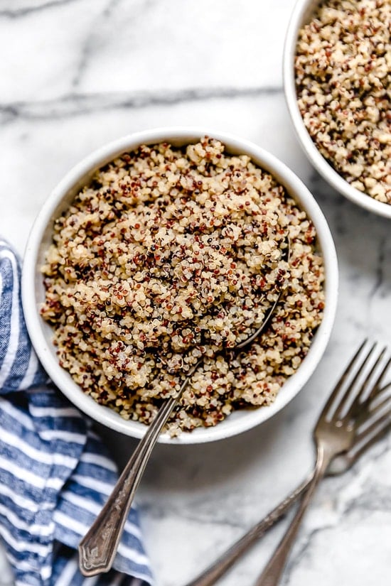 Learn how to cook perfect, fluffy Instant Pot quinoa! This hands-free method makes tender quinoa that's great in salads, bowls, and more. Overhead view of Instant Pot quinoa in a white bowl with a spoon for serving.