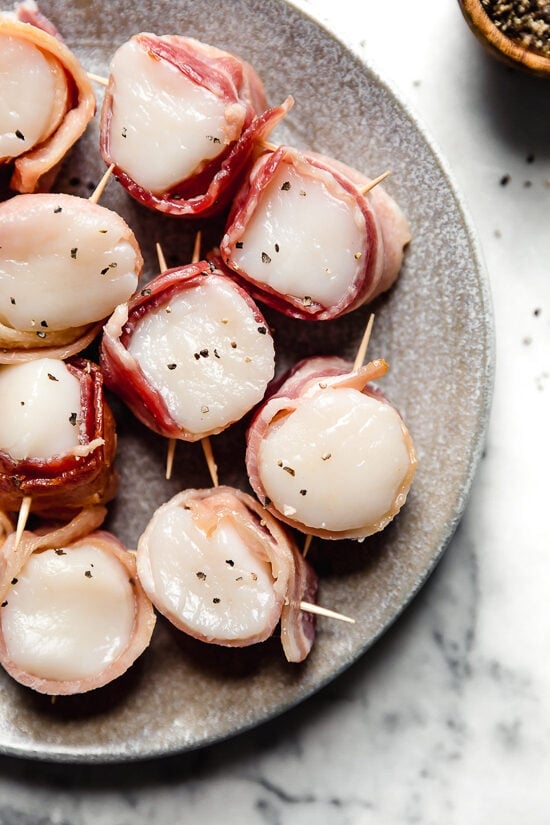 Partially cook bacon then wrap around the scallops using toothpicks to keep in place.