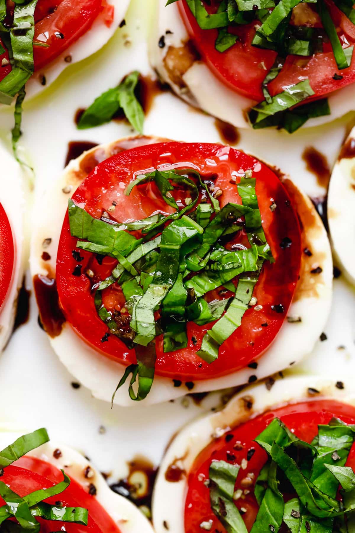 Caprese salad is a simple summer salad with fresh mozzarella, thick slices of juicy tomatoes, basil and a splash of balsamic vinegar. So easy! Overhead closeup of Caprese salad on platter