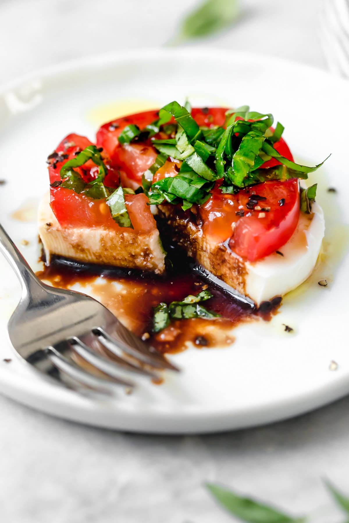 Caprese salad is a simple summer salad with fresh mozzarella, thick slices of juicy tomatoes, basil and a splash of balsamic vinegar. So easy! Caprese salad on plate with fork