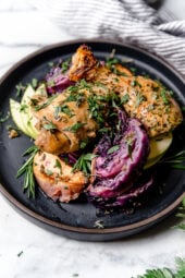 Baked apple cider chicken and red cabbage on a black plate.