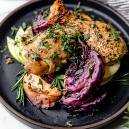 Baked apple cider chicken and red cabbage on a black plate.