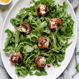 Prosciutto Wrapped Figs with Blue Cheese served on a bed of baby arugula with a light vinaigrette. A delicious combination of salt, acid and sweet.