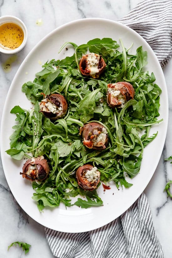 Prosciutto Wrapped Figs with Blue Cheese served on a bed of baby arugula with a light vinaigrette. A delicious combination of salt, acid and sweet.