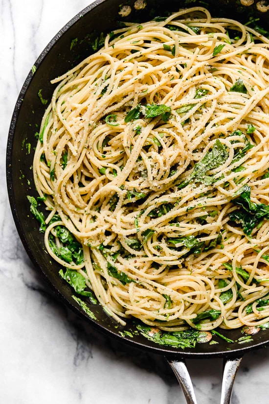 With diced bacon, grated cheese, black pepper, and a poached egg, this Spaghetti Carbonara is simple yet elegant. Spaghetti in a skillet with greens