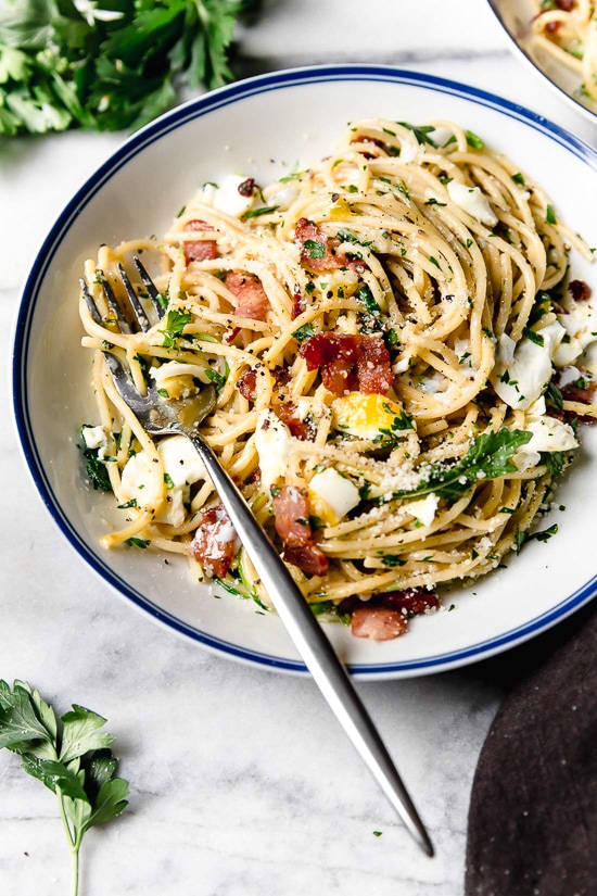 With diced bacon, grated cheese, black pepper, and a poached egg, this Spaghetti Carbonara is simple yet elegant. A fork sitting on a bowl of spaghetti carbonara