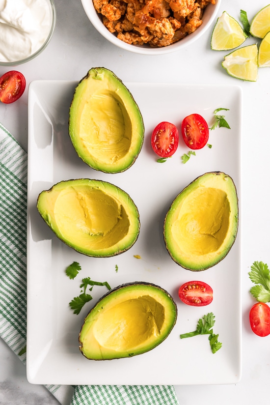 Avocados on a plate hollowed out and ready to stuff.
