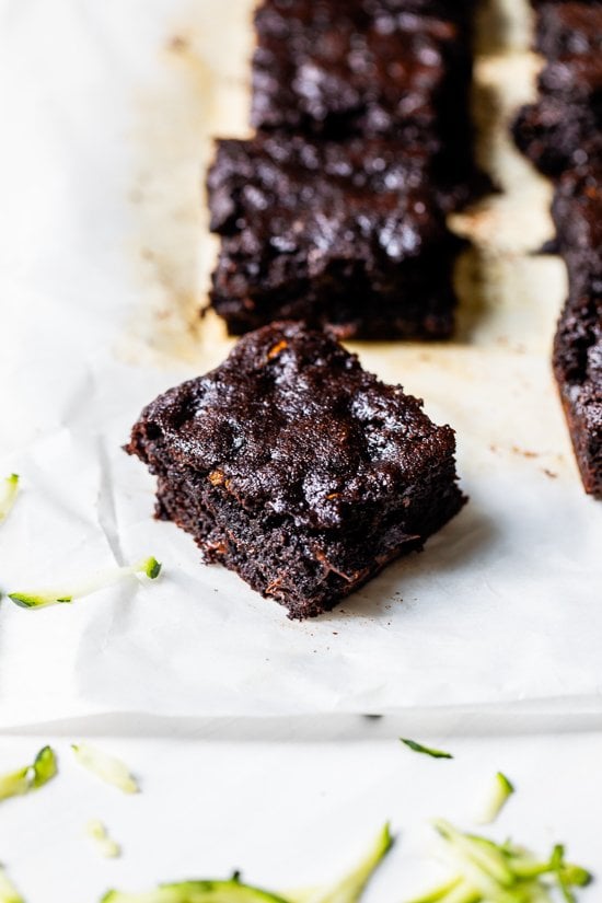 These easy Flourless Zucchini Brownies are made with almond meal, so they're naturally gluten-free. They're moist, fudgy, and so decadent! Flourless chocolate zucchini brownie on parchment paper, with additional brownies in background