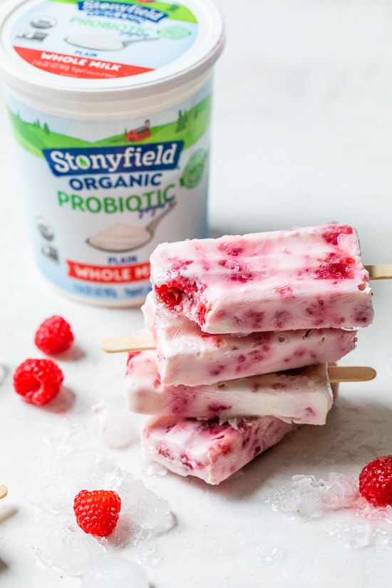 Raspberry Yogurt Ice Pops stacked with yogurt tub in background