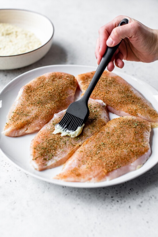 seasoned chicken breast with mayo being spreaded on top