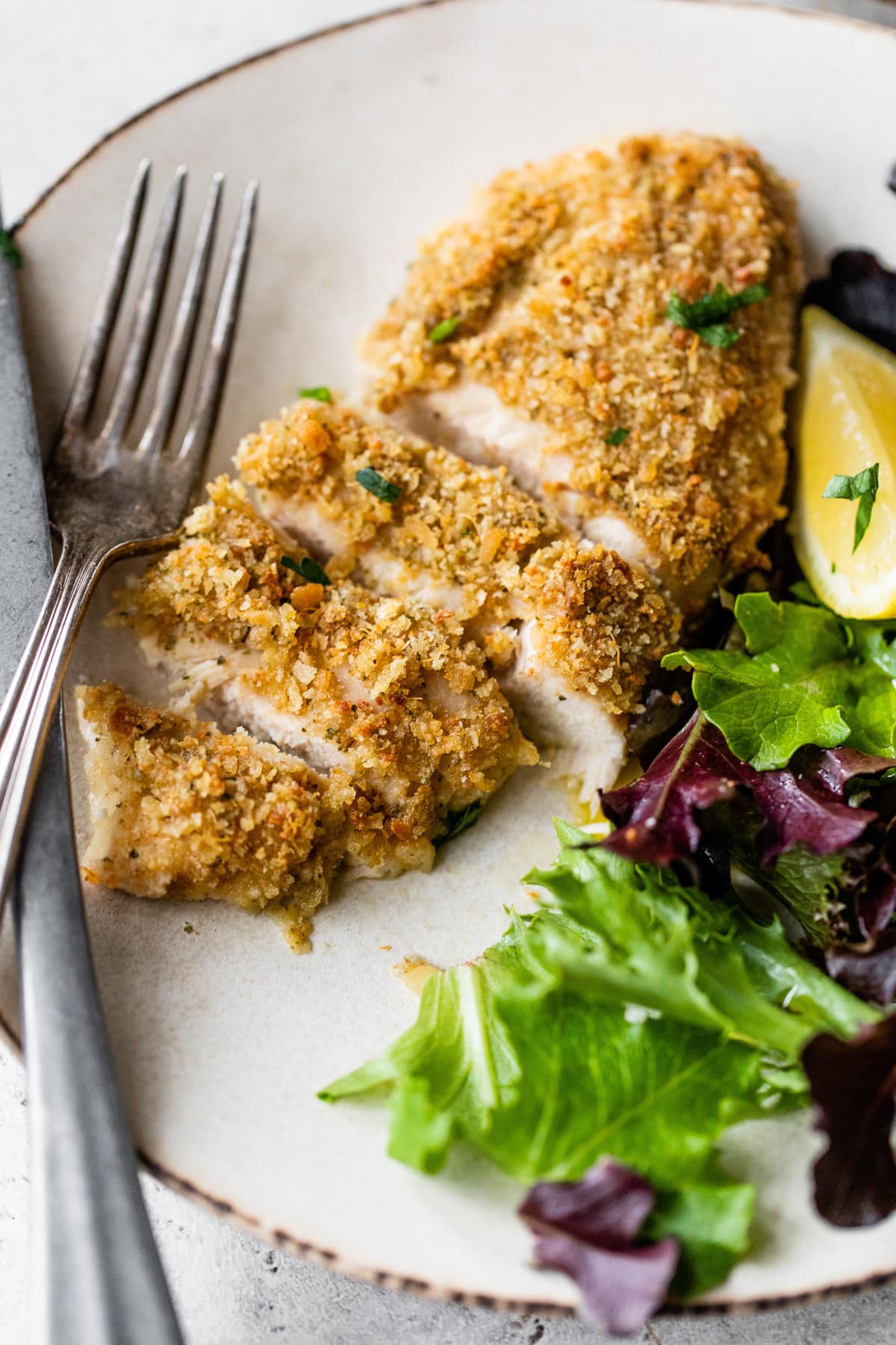cut up pieces of baked chicken breast with a side of romaine lettuce, a lemon, and a fork