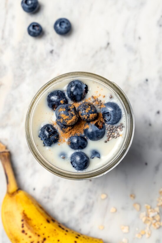 Overnight oats are the easiest way to work a healthy breakfast into your morning! No cooking required, they're a hearty breakfast packed with fiber, vitamins, and nutrients. Overhead view of overnight oats in jar with blueberries and cinnamon on top